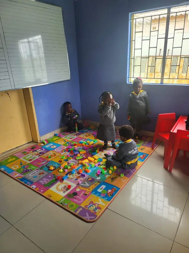 Nursery children playing with building blocks on a letter mat at the PHI campus