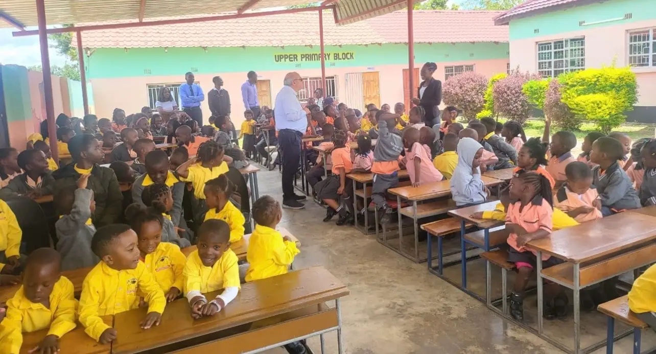 The whole school seated at benches under the covered area outside the upper primary block