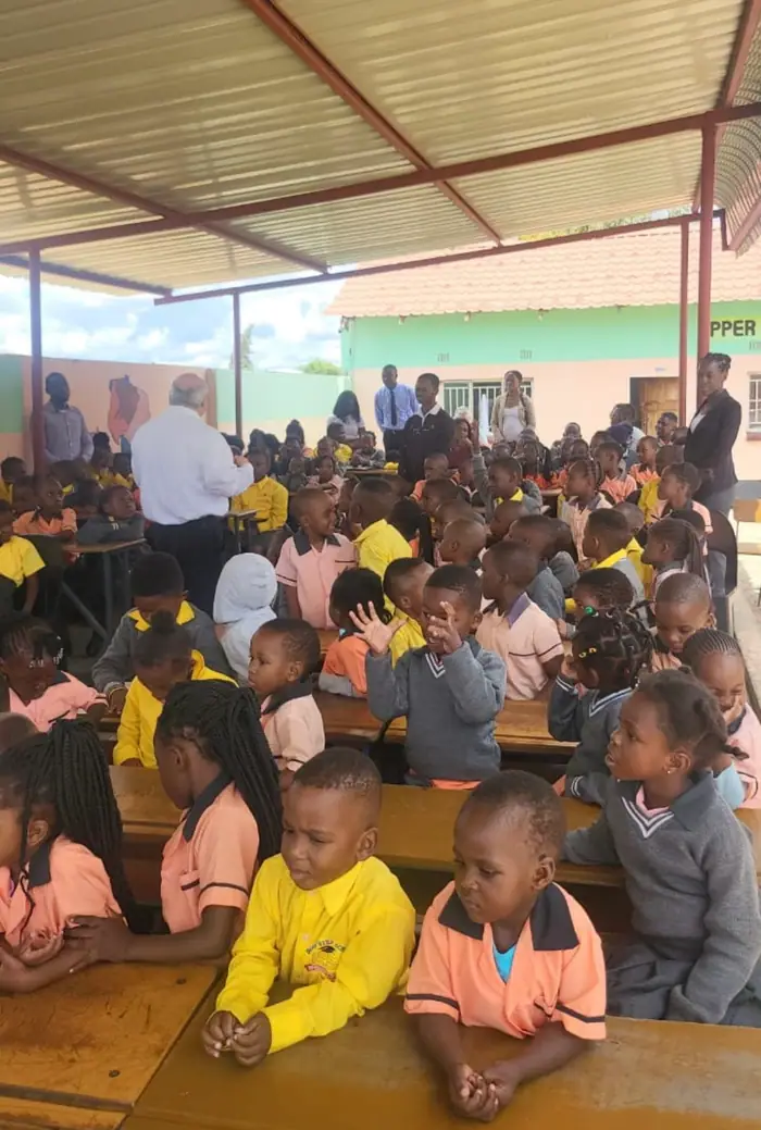 Younger pupils at the assembly, one of them waving at the camera